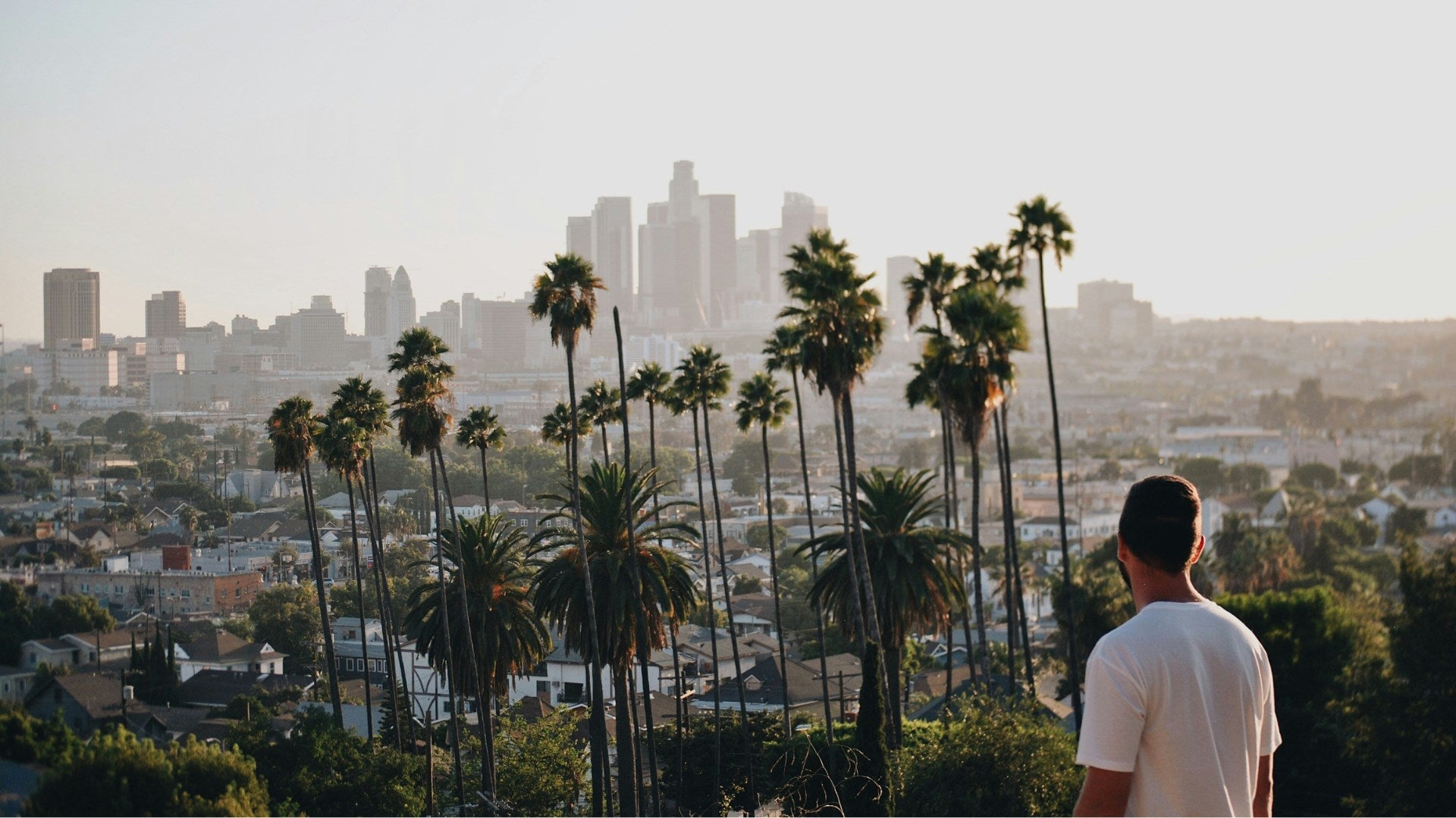 Un homme de dos regarde downtown Los Angeles depuis une colline.